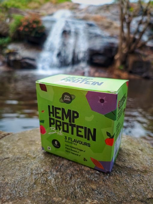 Hemp Protein Bites assorted box is kept on a scenic background of waterfall